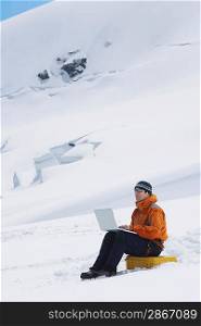 Hiker using laptop on snowy mountain peak