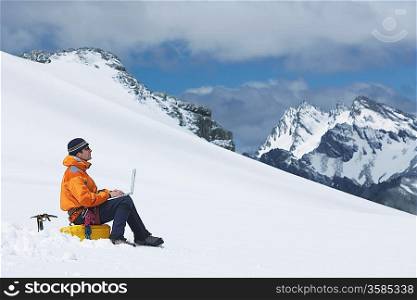 Hiker using laptop on snowy mountain peak
