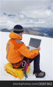 Hiker using laptop on snowy mountain peak back view