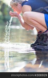 Hiker washing face with water from shallow stream
