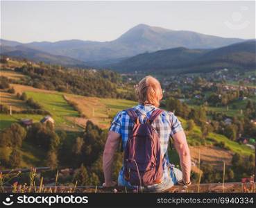 Hiker with backpack sitting on the fence enjoying mountain view