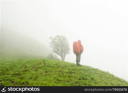 Hiker with backpack standing on top of a mountain and enjoying