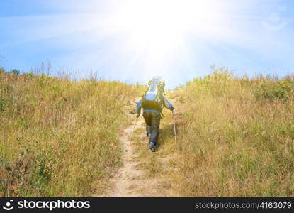 Hiker with rucksack up-hill at summer sunny day