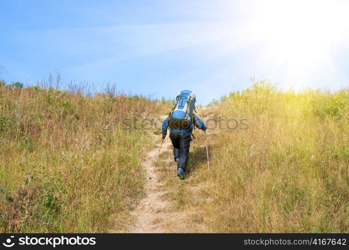 Hiker with rucksack up-hill at summer sunny day