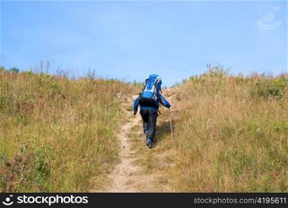 Hiker with rucksack up-hill at summer sunny day