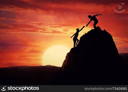 Hikers climbing on rock, mountain at sunset, one of them giving hand and helping to climb. Friendly assistance and support in a dangerous situation.