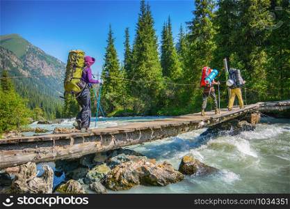 Hikers crossing over wood bridge under mountain river.