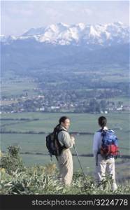 Hikers Standing On A Point Overlooking A Mountain Village