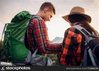 Hikers with backpacks looks on map, excursion in tourist town. Summer hiking. Hike adventure of young man and woman. Hikers looks on map, excursion in tourist town