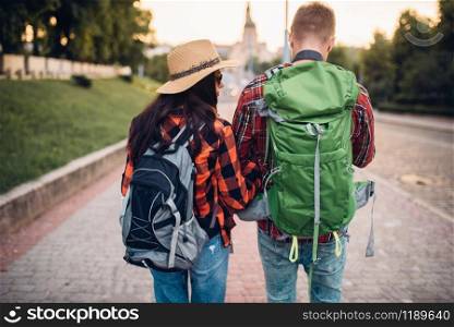 Hikers with backpacks on excursion in tourist town, back view. Summer hiking. Hike adventure of young man and woman. Hikers with backpacks on excursion, back view