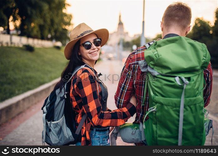 Hikers with backpacks on excursion in tourist town, back view. Summer hiking. Hike adventure of young man and woman