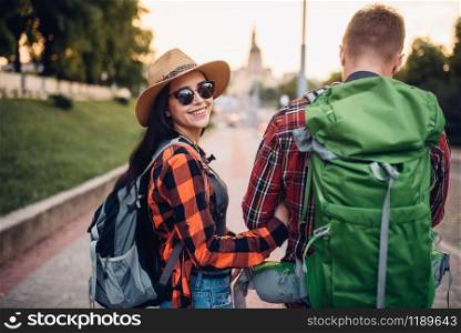 Hikers with backpacks on excursion in tourist town, back view. Summer hiking. Hike adventure of young man and woman