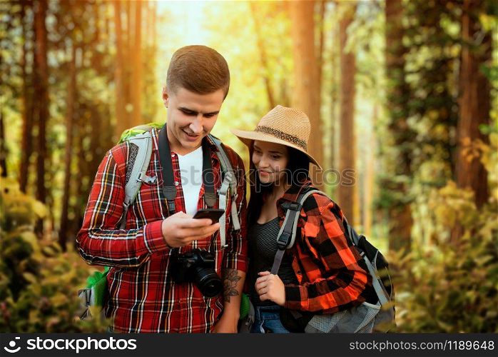 Hikers with backpacks traveling through the woods. Hiking in summer forest. Hike adventure of young man and woman