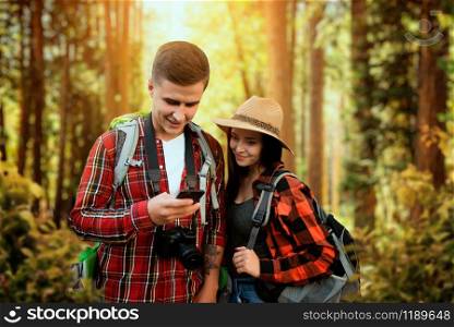 Hikers with backpacks traveling through the woods. Hiking in summer forest. Hike adventure of young man and woman