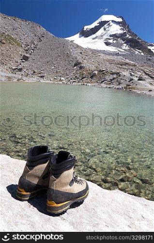 Hiking boots, back view, in background mountain landscape with lake and snowed peak (Gran Paradiso National Park, Italy).
