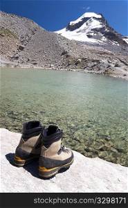Hiking boots, back view, in background mountain landscape with lake and snowed peak (Gran Paradiso National Park, Italy).