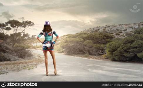 Hiking concept. Rear view of young woman standing aside of road