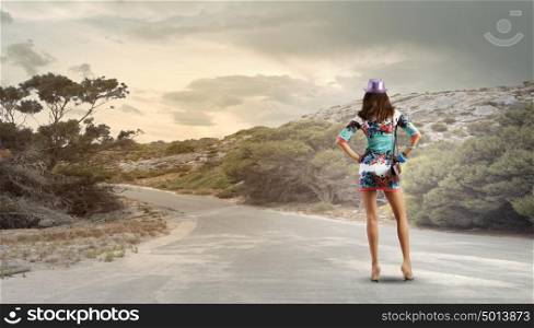 Hiking concept. Rear view of young woman standing aside of road