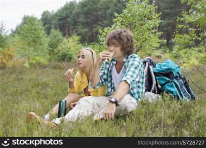 Hiking couple eating sandwiches while relaxing in field