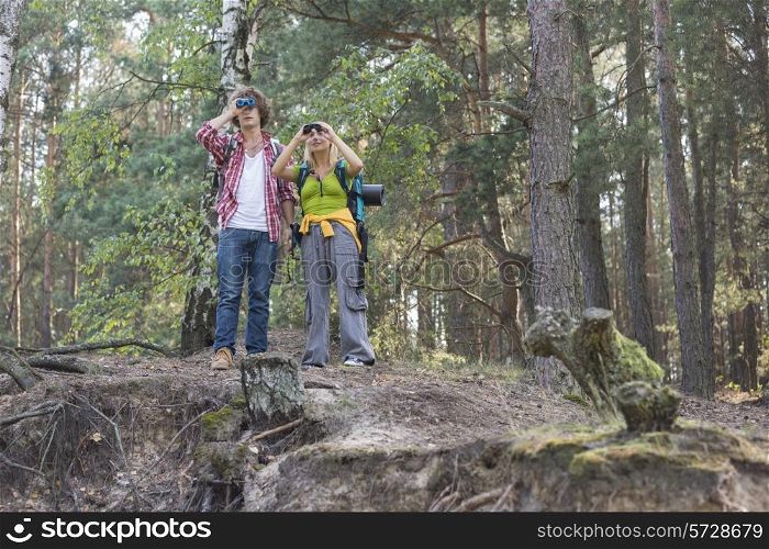 Hiking couple using binoculars in forest