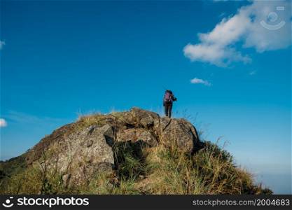 hiking girl standing with his back on the top of a tall rock beautiful blue sky