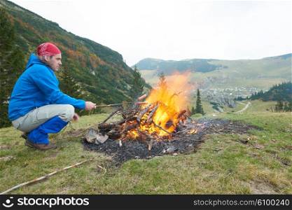 hiking man prepare tasty sausages on campfire in mountains