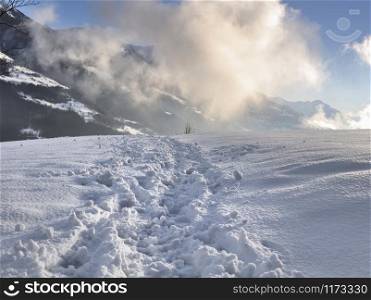 hiking path on the snow in mountain with clouds lightened by the sun