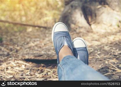 Hiking shoes young woman traveler sit down on summer park.focus on blue sneaker shoes and jeans on pathway. active activity vacation on hike mountain resting with walking way. Young traveler concept.