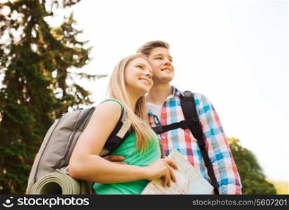 hiking, travel, vacation and friendship concept - smiling couple with map and backpack in nature