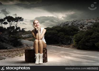 Hiking traveling. Young woman hiker sitting on suitcase along roadside