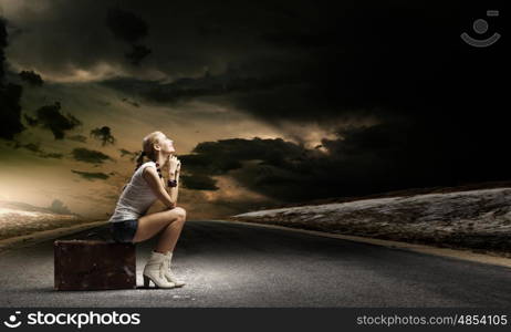 Hiking traveling. Young woman hiker sitting on suitcase along roadside