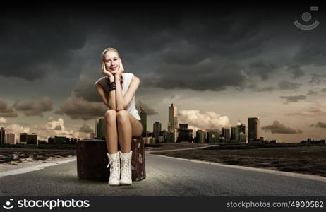 Hiking traveling. Young woman hiker sitting on suitcase along roadside