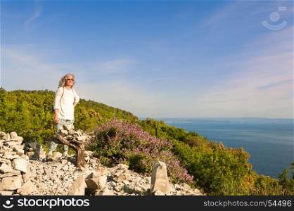 Hiking woman on cliff enjoying sunlit sea view.Female about 60 years old.Active retirement.Healthy lifestyle.