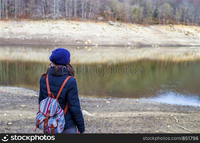 Hiking woman with backpack standing by the lake.