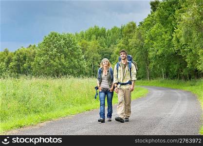 Hiking young couple backpack tramping on asphalt road countryside