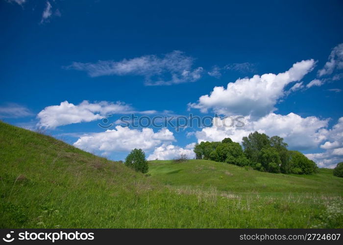 Hill and green meadow under cloudy sky