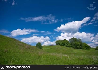 Hill and green meadow under cloudy sky