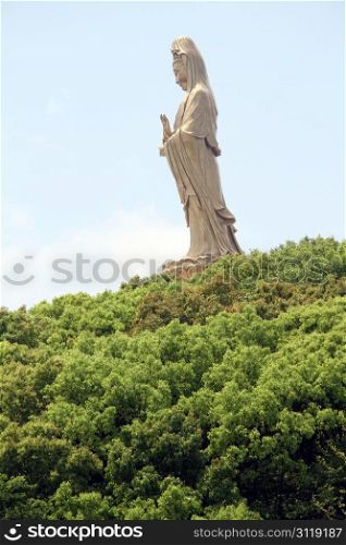 Hill with green trees and statue of Guan Yin on the Putoshan island, China
