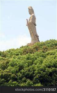 Hill with green trees and statue of Guan Yin on the Putoshan island, China