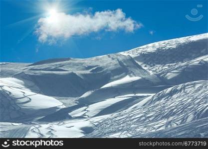 Hillside freaked ski tracks with sunshine and lonely cloud in the blue sky. Winter Austria.