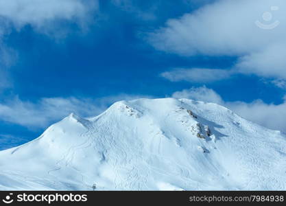 Hillside undulate ski tracks and clouds in the blue sky. Winter Austria.