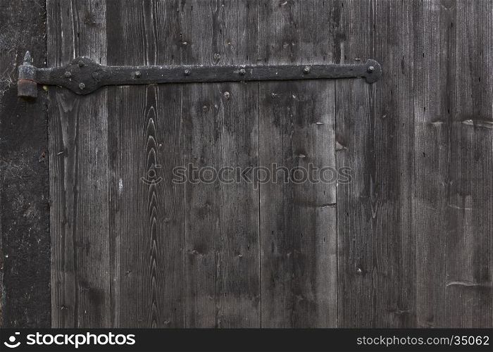 hinge and part of shed door consisting of old vertical wooden planks with faded black or grey paint