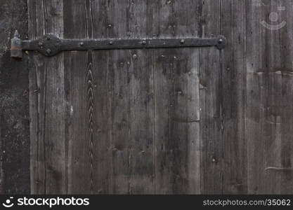 hinge and part of shed door consisting of old vertical wooden planks with faded black or grey paint