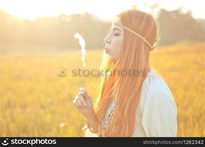 Hippie beautiful woman blowing flower on the golden meadow