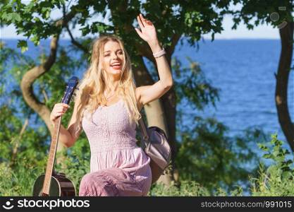 Hippie looking young adult woman wearing gypsy outfit having acoustic guitar. Female playing music in park.. Woman playing acoustic guitar in park