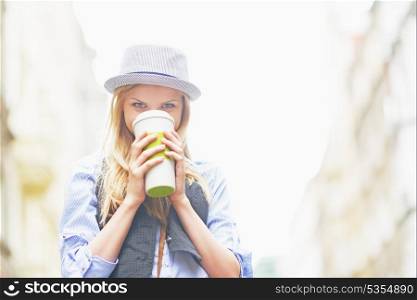 Hipster girl drinking hot beverage on city street