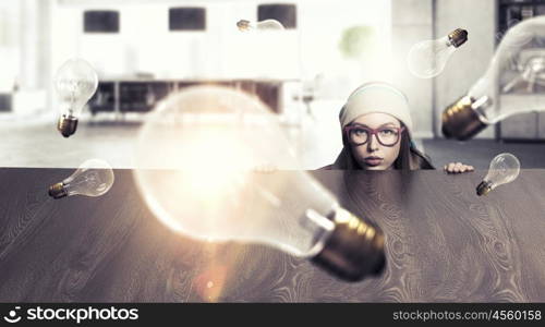 Hipster girl looking from under table. Attractive student girl in red glasses peeping from under table