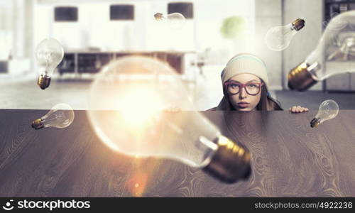 Hipster girl looking from under table. Attractive student girl in red glasses peeping from under table