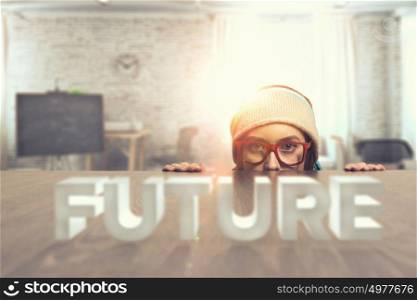 Hipster girl looking from under table. Attractive student girl in red glasses peeping from under table