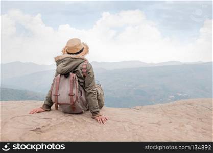 Hipster girl sitting in rocky of mountain . Hipster girl with backpack sitting in a rocky top of the mountain against the blue of sky